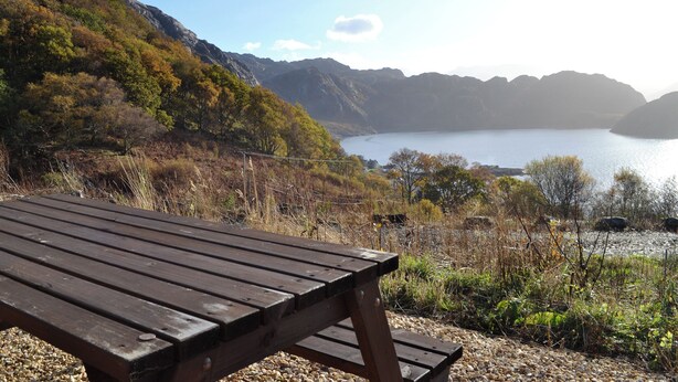 Un banco de madera con vistas a un lago y montañas al fondo.