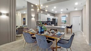 A modern kitchen with white cabinets, a central island, and a dining area with a glass table and chairs.