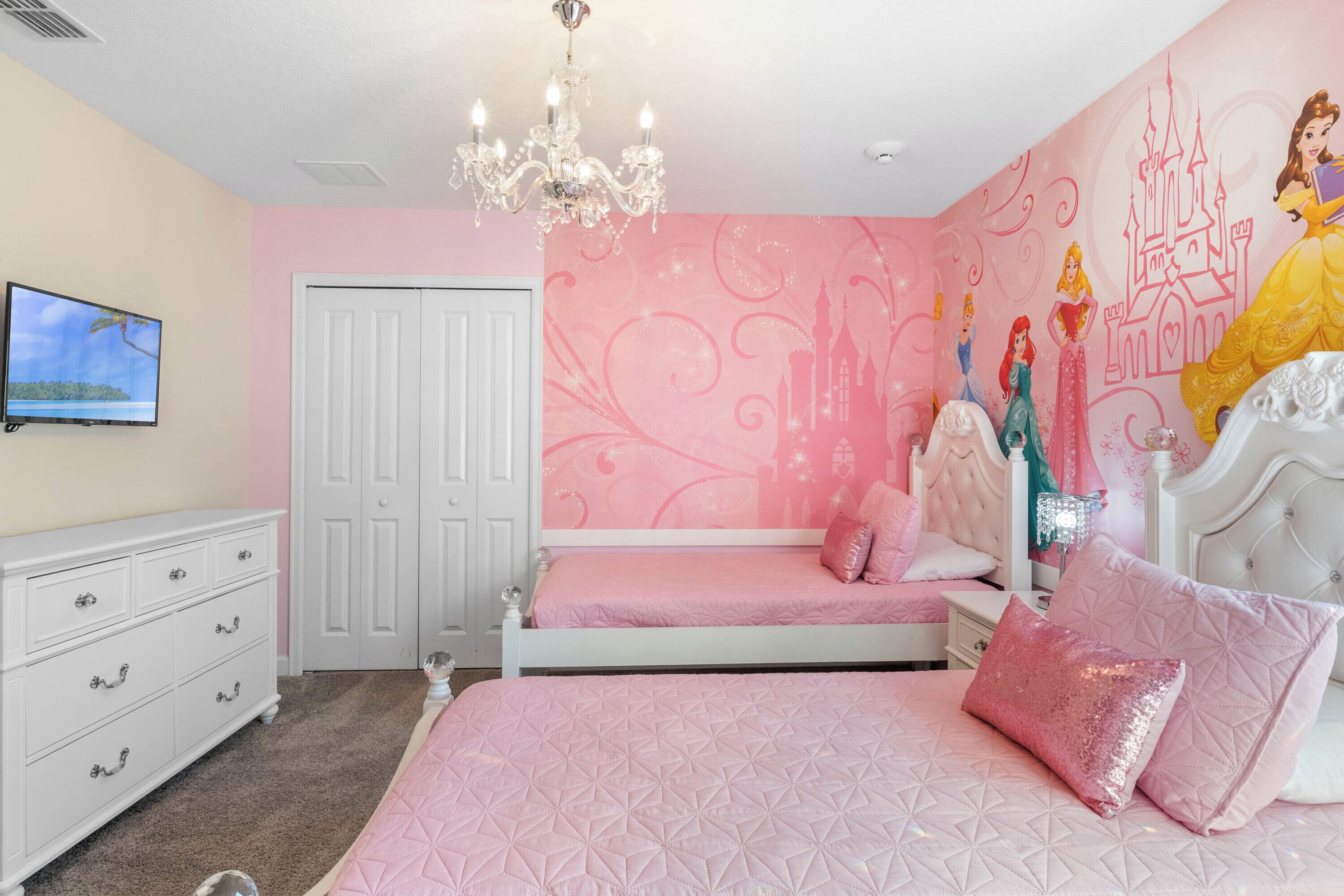 A bedroom with a bed, a dresser, a vanity, a chandelier, and a wall mural.