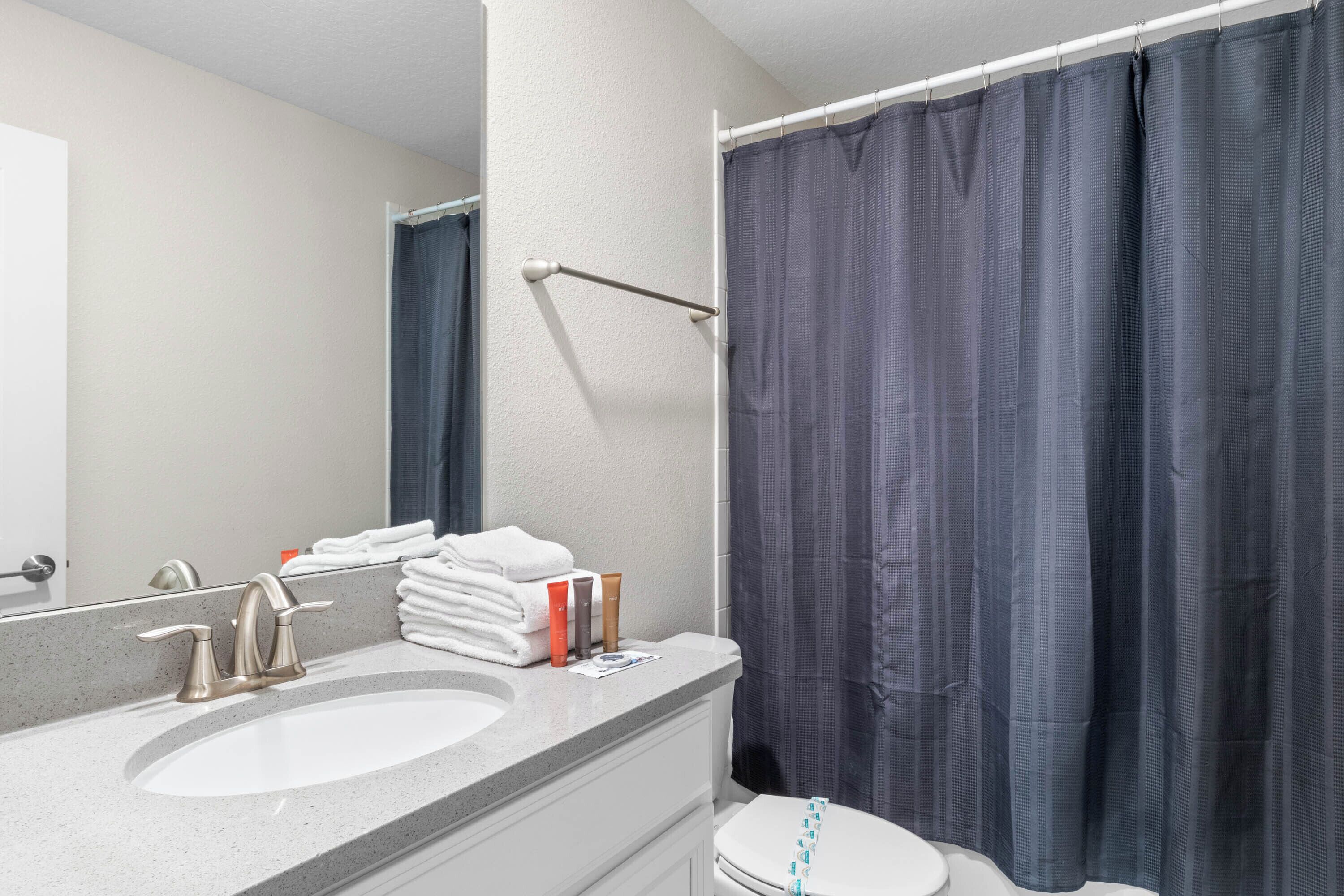 Een badkamer met een wastafel, spiegel, handdoekhouder en douchegordijn.