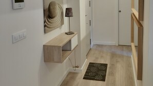A hallway with a wooden floor, a black rug, a wall-mounted light, a thermostat, and a door. - NON STRESS: Charming apartment (València)