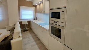 A modern kitchen with white cabinets, a built-in oven, microwave, and a window with blinds. - NON STRESS: Charming apartment (València)