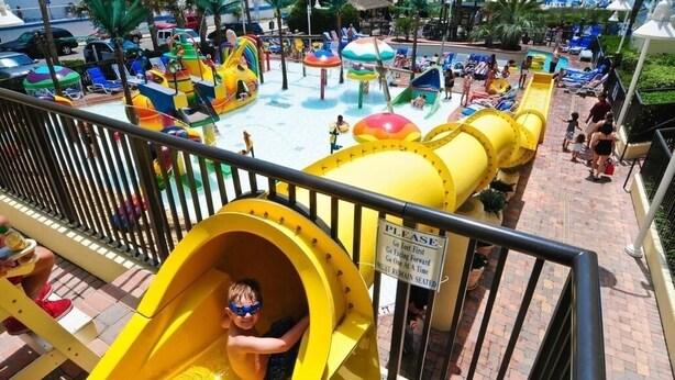 Un parc aquatique doté d ’un toboggan jaune et de diverses structures ludiques aquatiques.