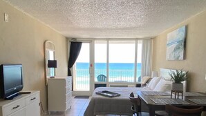 A hotel room with a bed, a desk, a chair, a TV, a small table, a plant, and a view of the ocean. - Cute Studio!  Remodeled!  Direct Ocean Front! Pirates Cove 6th Floor (Daytona Beach)