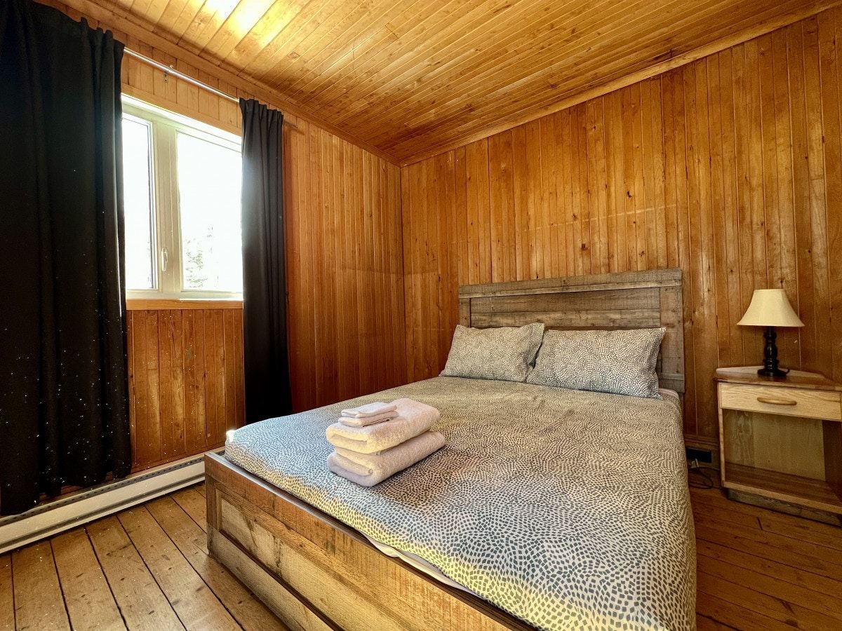 A wooden-paneled bedroom with a bed, a nightstand, and a window with curtains.