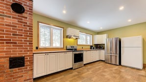 A kitchen with white cabinets, a brick wall, and a stainless steel refrigerator. - 2355/2 · Villa des pins (Saint-Gabriel-de-Valcartier)