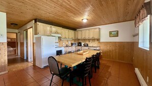 A kitchen with wooden cabinets, a large island, and a dining area with chairs. - Cottage Montagne - Vallée Jeunesse site (Saint-Gabriel-de-Valcartier)