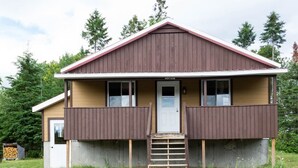 A two-story wooden building with a brown roof and a white door. - Cottage Montagne - Vallée Jeunesse site (Saint-Gabriel-de-Valcartier)