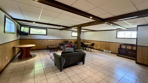 A spacious room with a large sofa, a wooden table, and a fireplace. - Cottage Montagne - Vallée Jeunesse site (Saint-Gabriel-de-Valcartier)