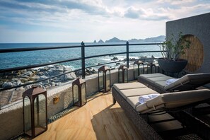 Un espacio al aire libre con sol, sillas reclinables y una planta en maceta, con vista a un litoral rocoso y el mar.