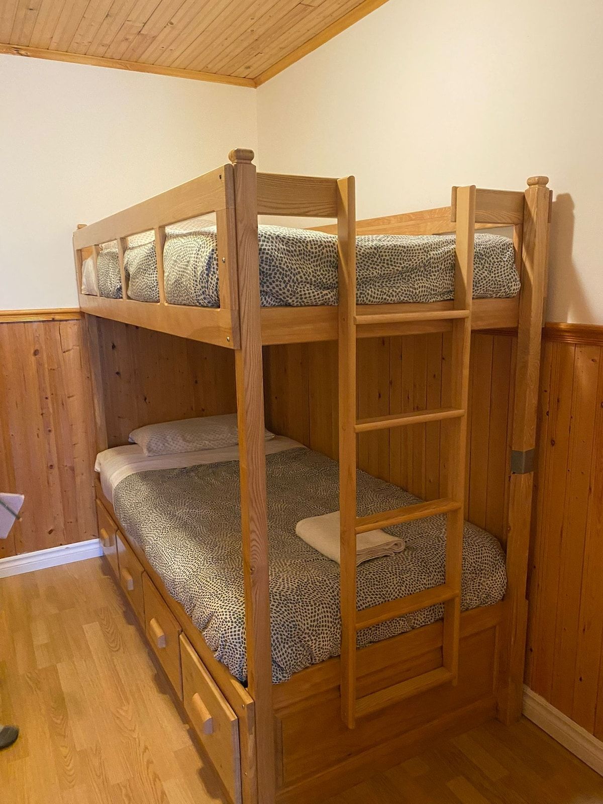 A bunk bed with a ladder, wooden walls, and a wooden floor.