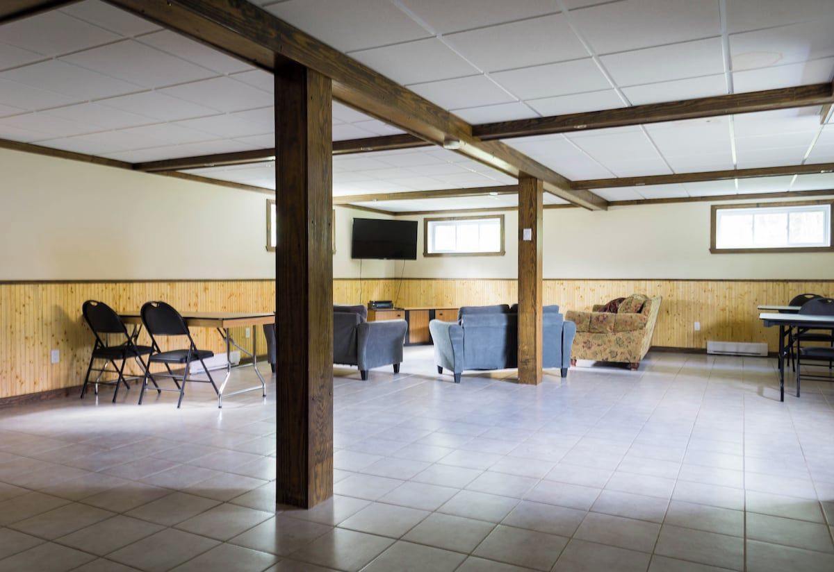A spacious room with a high ceiling, wooden beams, a flat-screen TV mounted on the wall, and several seating options including chairs and sofas.