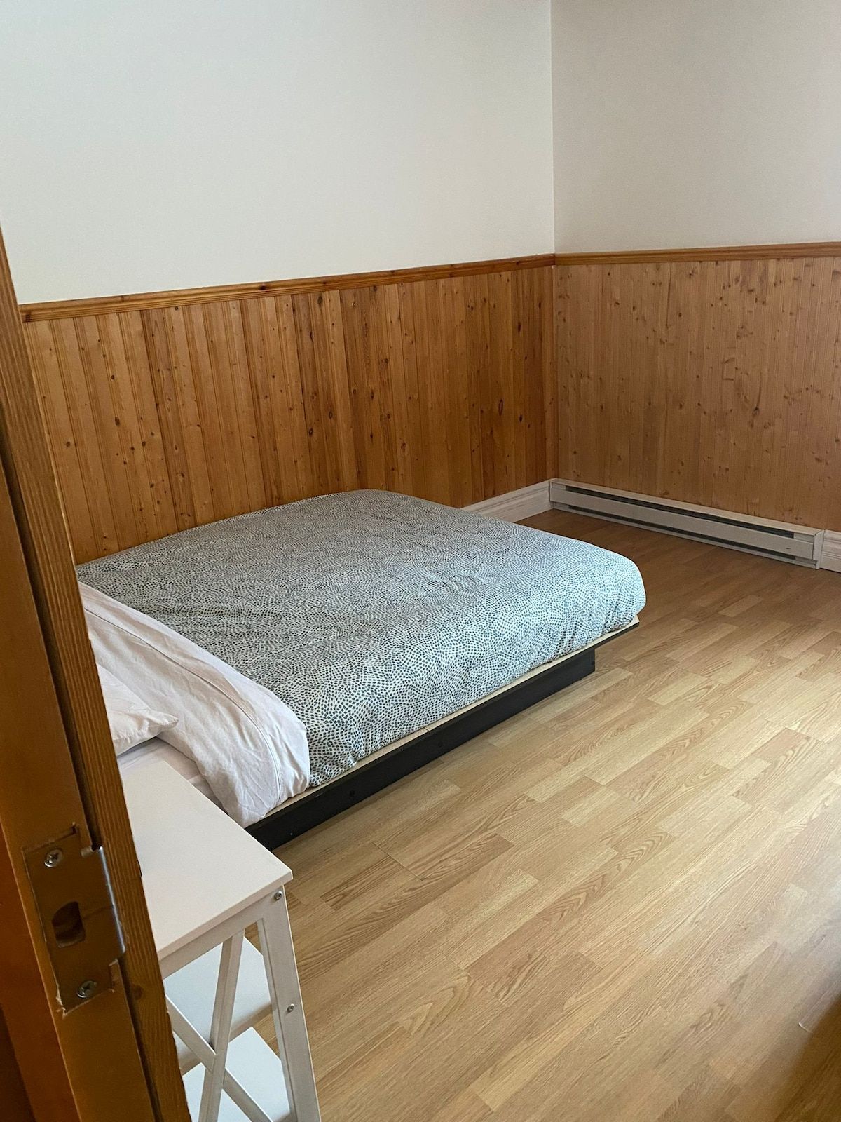 A room with a single bed, wooden panel walls, and a white table.