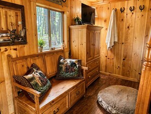 Interior de una cabaña con un banco de madera, un televisor y un armario.