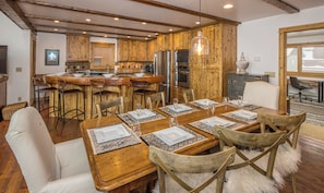 A wooden interior with a dining table set for six, kitchen appliances, and a bar area.