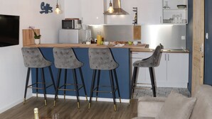 Eine moderne Küche mit Barhocker, einem Esstisch mit einer Champagnerflasche und einem Sofa im Wohnbereich.