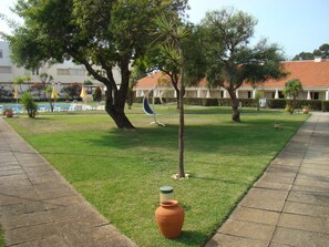 A well-maintained grassy area with a large tree, a swing, and a decorative pot. - Clube Pinhal Da Foz (Esposende)