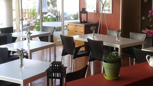 A restaurant interior with multiple tables and chairs, a coffee machine, and a view of the outdoors through large windows. - Clube Pinhal Da Foz (Esposende)
