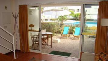 A room with a sliding glass door leading to an outdoor area with a pool, chairs, and umbrellas.