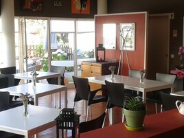 Interior de un restaurante con varias mesas y sillas, una máquina de café y vistas al exterior a través de grandes ventanales.