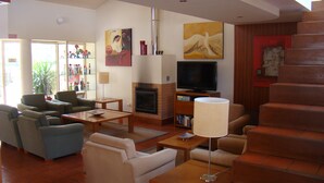 A spacious living room with a fireplace, a television, and a staircase. - Clube Pinhal Da Foz (Esposende)