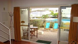 A room with a sliding glass door leading to an outdoor area with a pool, chairs, and umbrellas. - Clube Pinhal Da Foz (Esposende)