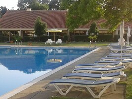 Una piscina con sillas de descanso y sombrillas, rodeada por un edificio con techo de tejas.