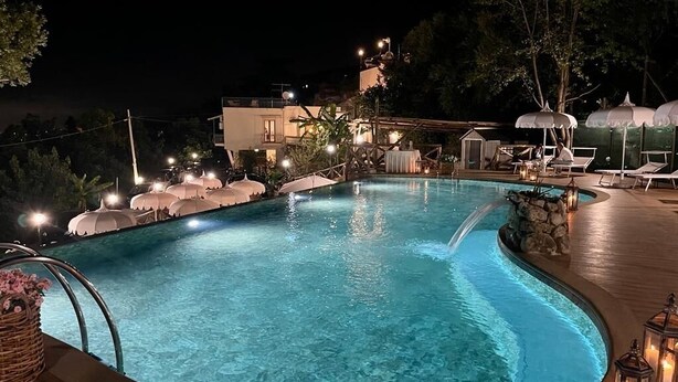 A nighttime swimming pool with lounge chairs and umbrellas, surrounded by trees and a building. - Casa Paola 2 (Vico Equense)