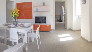 A modern kitchen with white and orange cabinets, a dining table set with chairs, and a vase of flowers. - Casa Paola 2 (Vico Equense)