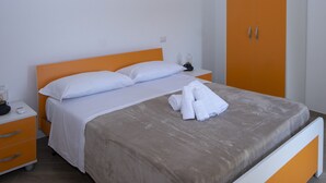 A neatly made bed with white linens and a grey duvet, a bedside table with a lamp, and an orange wardrobe with two doors. - Casa Paola 2 (Vico Equense)