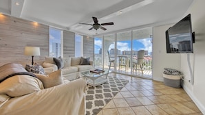 A spacious living room with a sofa, coffee table, and a balcony with a view of the city. - Dolphin Point 502B | Harbor front Views + Pool | Near Beach | Amenity Perks (Destin)