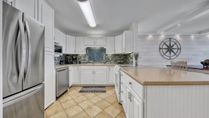 A kitchen with white cabinetry, a stainless steel refrigerator, a tiled backsplash, and a wooden island with a countertop. - Dolphin Point 502B | Harbor front Views + Pool | Near Beach | Amenity Perks (Destin)