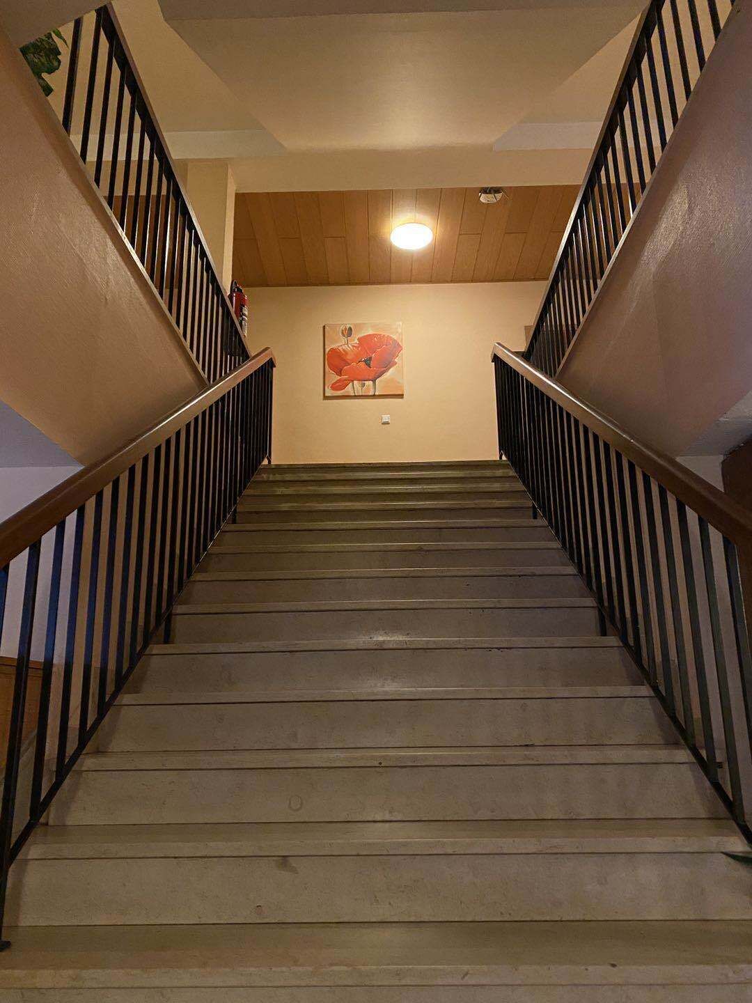 A wooden staircase with black railings, a wooden ceiling, and a wall-mounted light fixture.