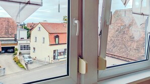Una ventana con cortinas blancas y vistas a una calle con edificios y coches aparcados.