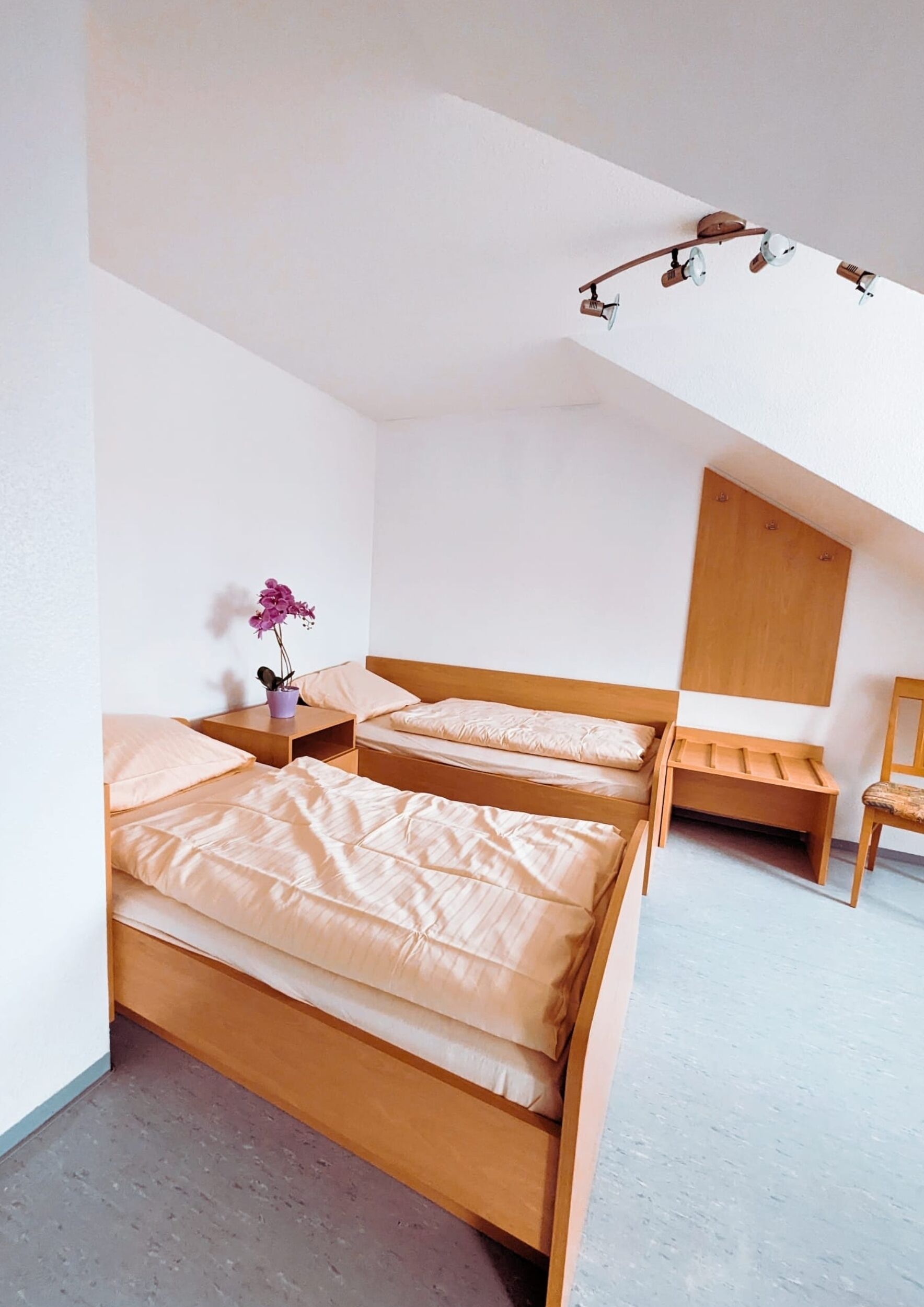 Un dormitorio con dos camas de madera, una mesita de noche con un jarrón morado y una silla de madera.