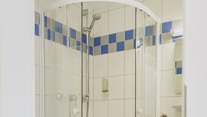 Una ducha con paredes de vidrio, diseño curvo, paredes de azulejos blancos y ubicada en una esquina.