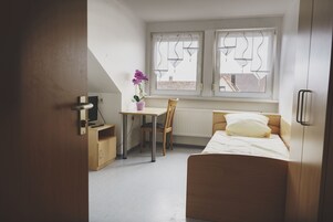 A bedroom with a bed, a desk, a chair, and a window with blinds.