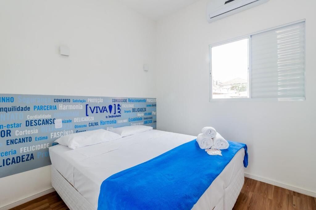 Een hotelkamer met een bed, een blauwe deken en een raam met zonwering.