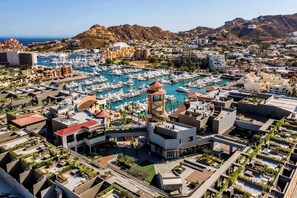 An aerial view of a marina with numerous boats, surrounded by modern buildings with rooftop gardens and a prominent tower structure. - Paraiso Marina View | Cabo Marina Oceanview Condo (Cabo San Lucas)