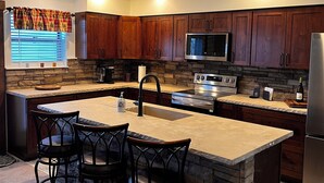 A modern kitchen with wooden cabinets, a central island with bar stools, a built-in microwave, and a stainless steel refrigerator. - Charming Rustic Townhome in the Heart of the Villages at Seven Springs (Champion)