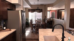 A modern kitchen with a central island, built-in appliances, and a dining area in the background. - Charming Rustic Townhome in the Heart of the Villages at Seven Springs (Champion)