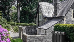 Une maison en pierre avec un toit en pente, entourée d’un jardin bien entretenu, agrémenté de fleurs violettes et d’une clôture en bois.