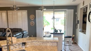 A kitchen with a granite countertop, dark wooden cabinets, and a sink. There is a dining area with a table and chairs visible through an open door. - It’s AZ Time...Relax in a private heated pool, Golf, Spring Training, Hiking! (Surprise)