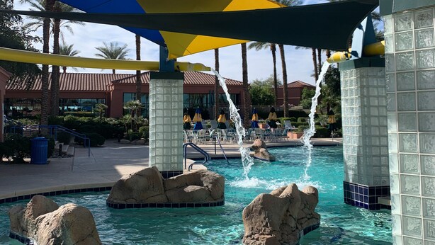 A pool area with clear water, rock formations, and umbrellas. - It’s AZ Time...Relax in a private heated pool, Golf, Spring Training, Hiking! (Surprise)
