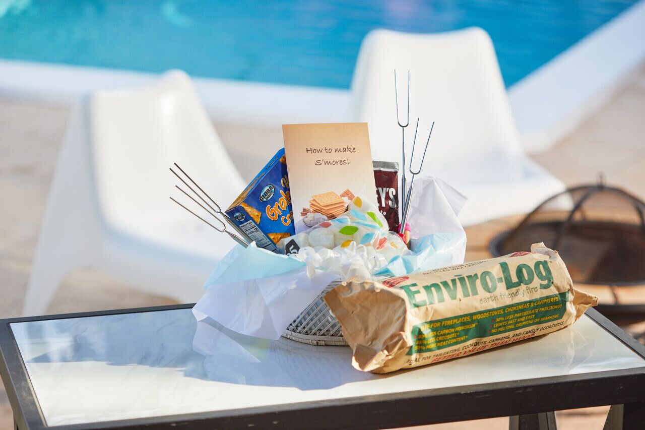 A poolside table with a bag of Enviro-Log firewood, a card titled "How to make S'mores!", and a box of graham crackers.