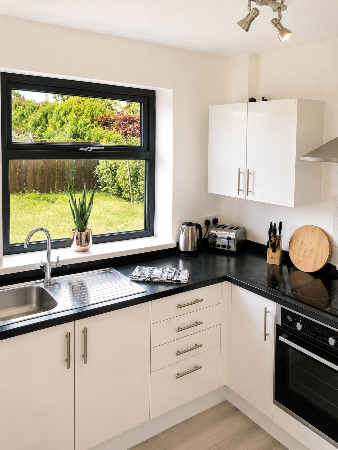 A modern kitchen with a black countertop, stainless steel appliances, and a window with a view of greenery.