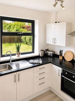 A modern kitchen with a black countertop, stainless steel appliances, and a window with a view of greenery. - HC Property - Mountford (Durham)