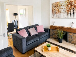 A modern living room with a dark grey sofa, two pink cushions, a wooden coffee table with a plant, and a fireplace. - HC Property - Mountford (Durham)