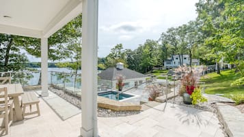 A covered patio with a pool, outdoor furniture, and a view of a lake and houses.