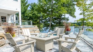 Une terrasse extérieure avec une table et des chaises en pierre, donnant sur un lac et entourée d’arbres.